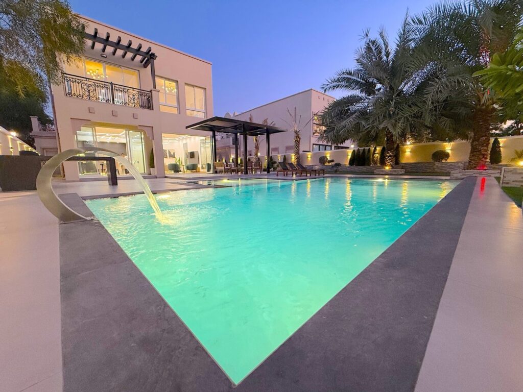 Villa pool lit at dusk with a curved water feature and pergola