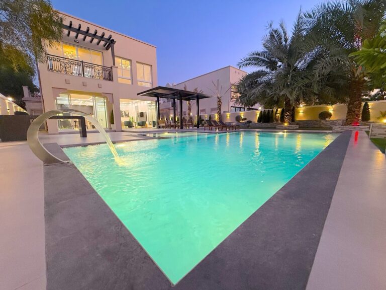 Villa pool lit at dusk with a curved water feature and pergola