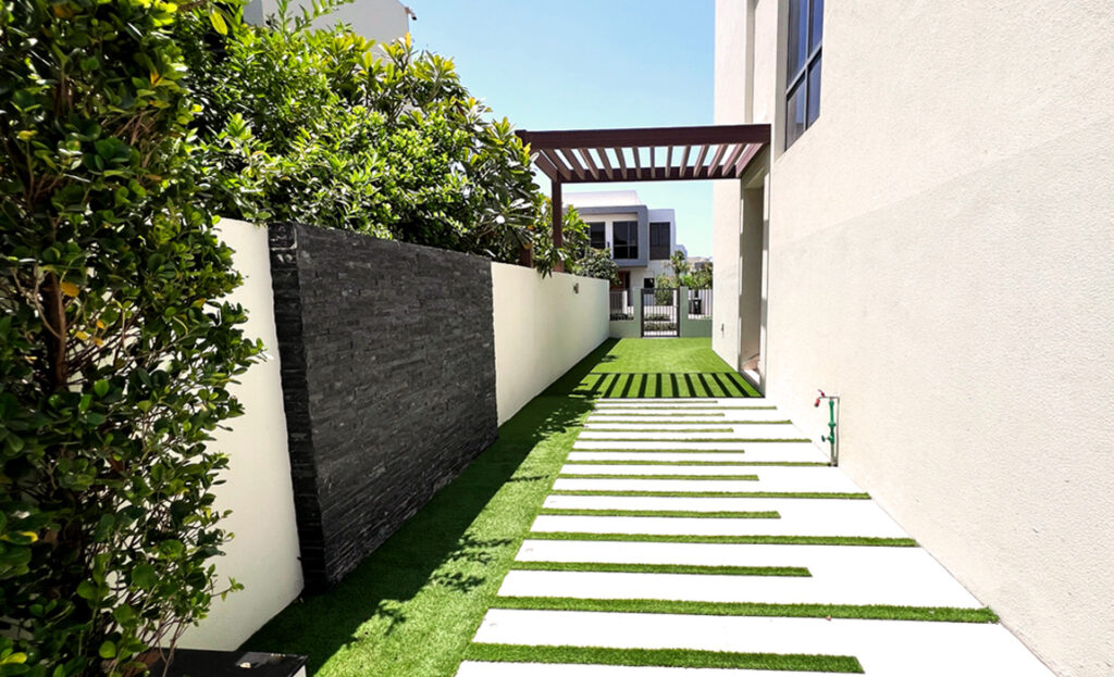 Stepping-stone path and turf beside a villa wall with a pergola at the end, Dubai Hills Villa 174